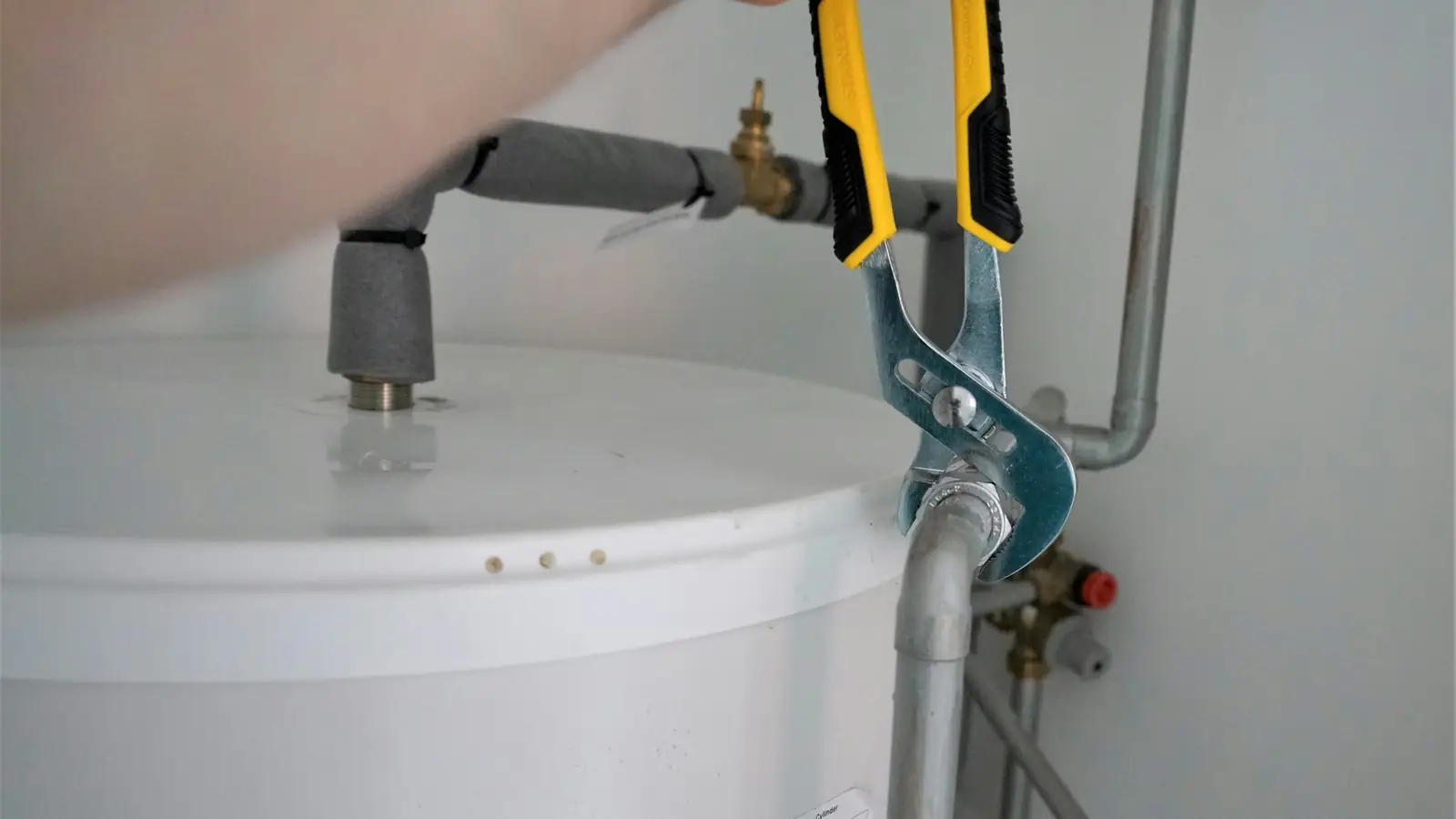 Main serrant un raccord sous un chauffe-eau électrique blanc
